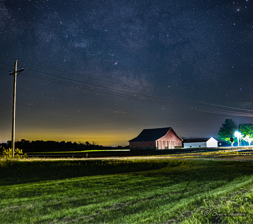 Milky Way over barn in rural Indiana. Car approaching from right, illuminated barn and light pole